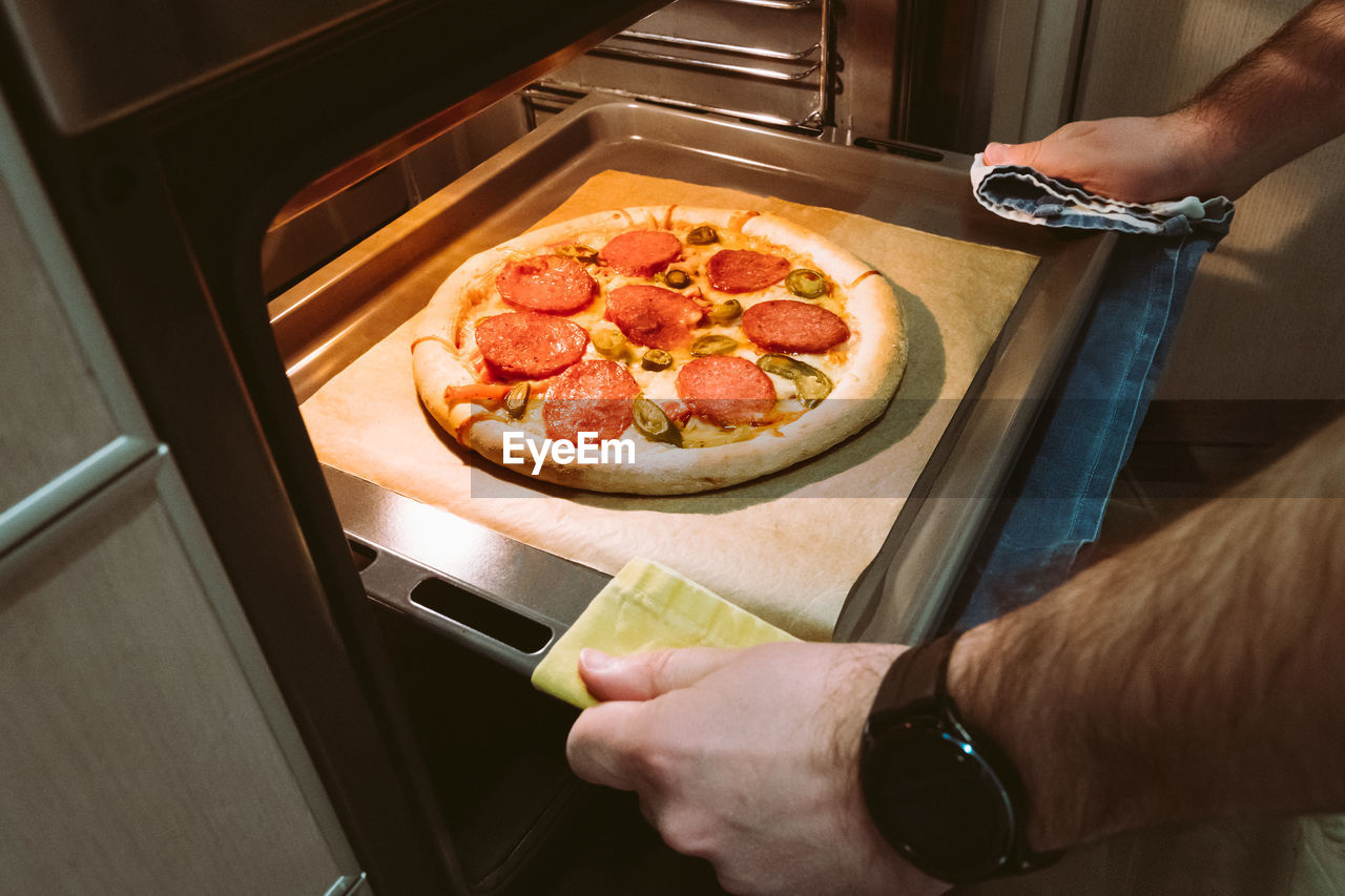 A man pulls a tray of pepperoni pizza from the oven at home