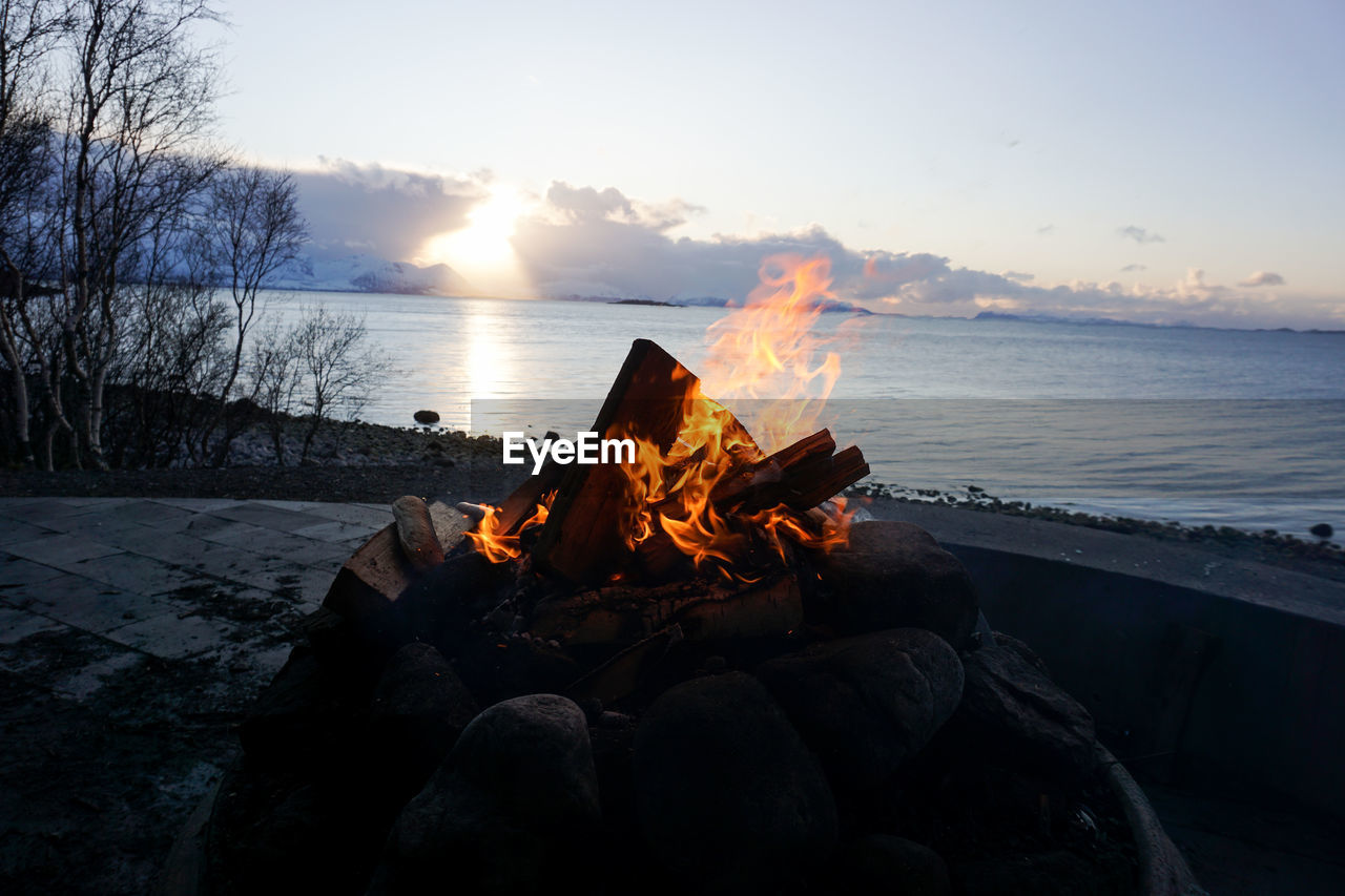 Bonfire on wooden log against sky during sunset