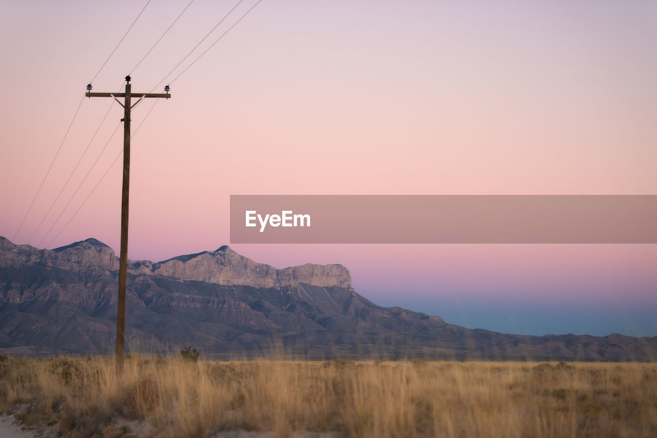 sky, electricity, landscape, environment, technology, mountain, nature, cable, scenics - nature, sunset, beauty in nature, electricity pylon, power generation, land, no people, power supply, dawn, power line, tranquility, mountain range, tranquil scene, outdoors, rural scene, plant, non-urban scene, evening, grass, remote, desert, horizon, travel destinations, twilight, pink, clear sky, prairie, travel, winter, silhouette, copy space, transmission tower, architecture