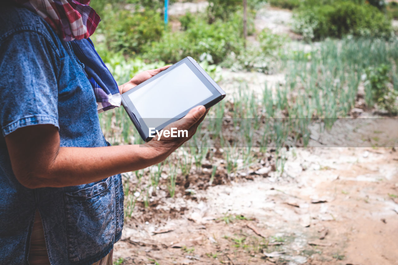 Midsection of man using digital tablet while standing on field