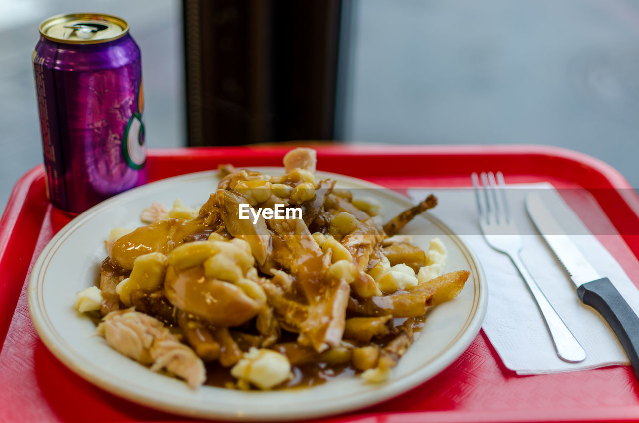 High angle view of chicken poutine served in plate with drinking can on tray