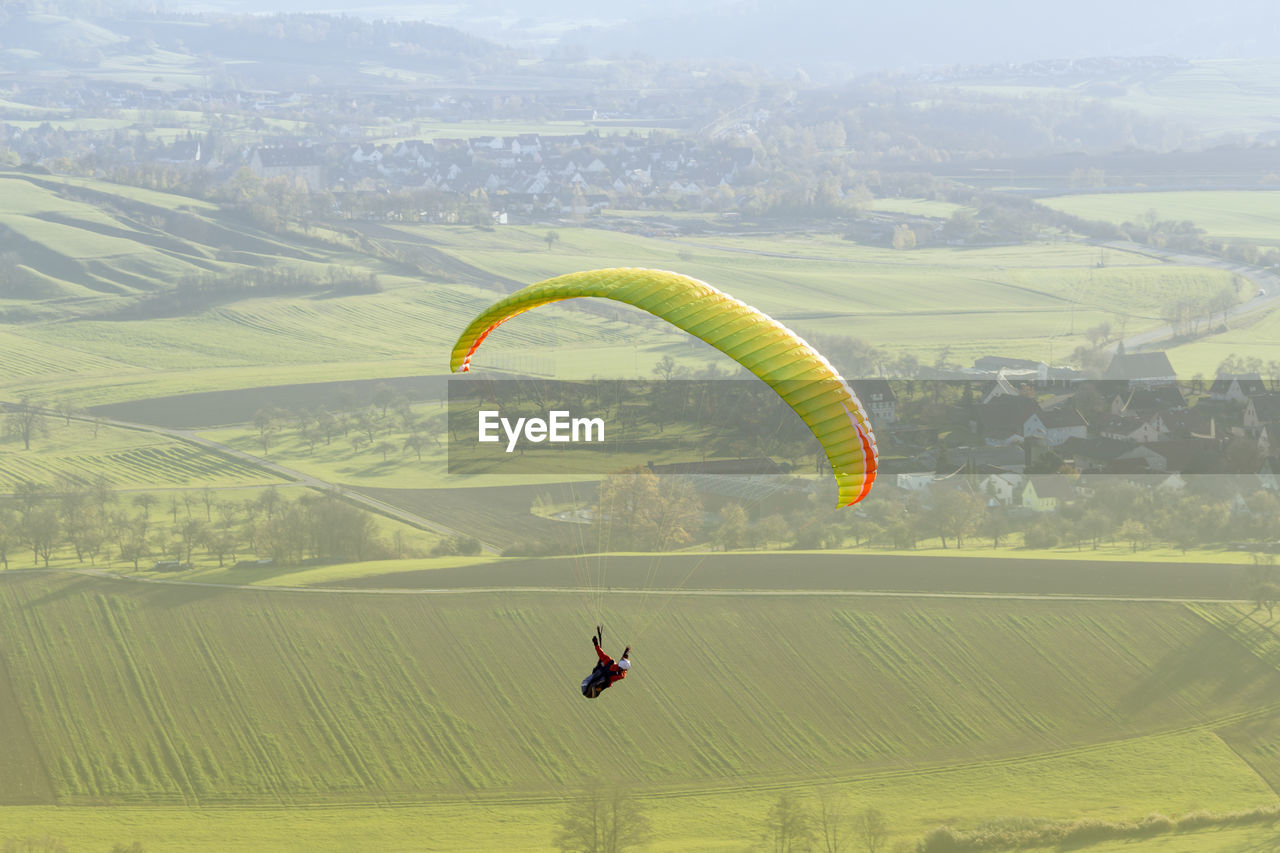 PERSON PARAGLIDING AGAINST GREEN LANDSCAPE