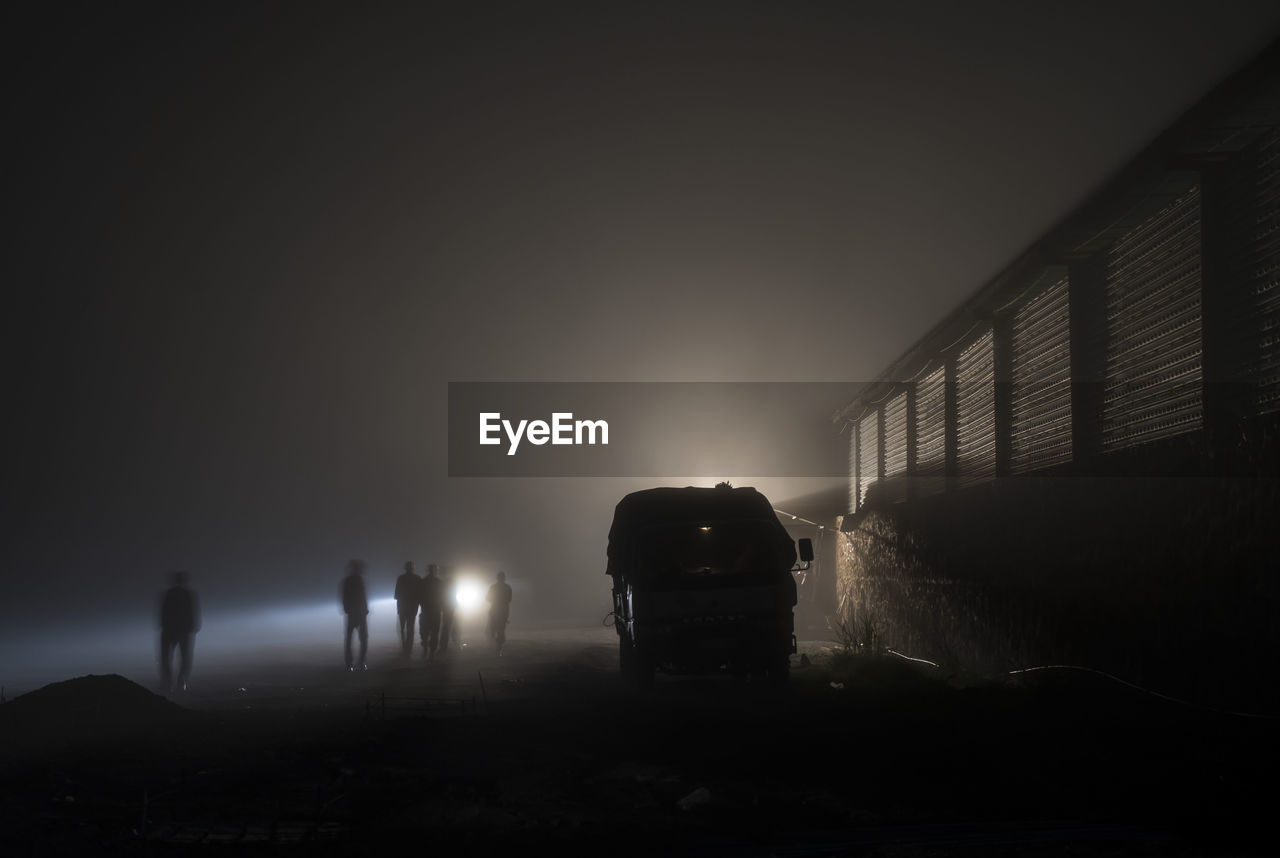 People walking by building against sky during foggy weather at night