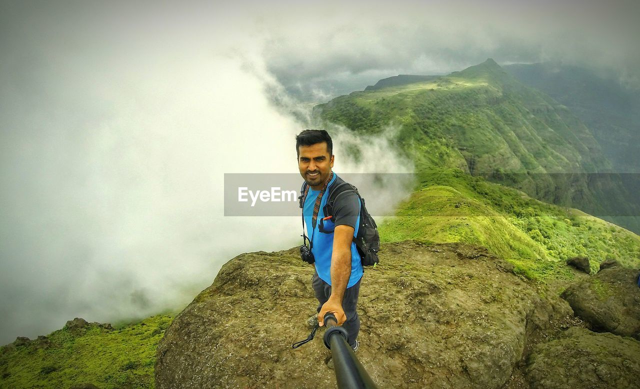 High angle view of young man taking selfie on mountain against clouds