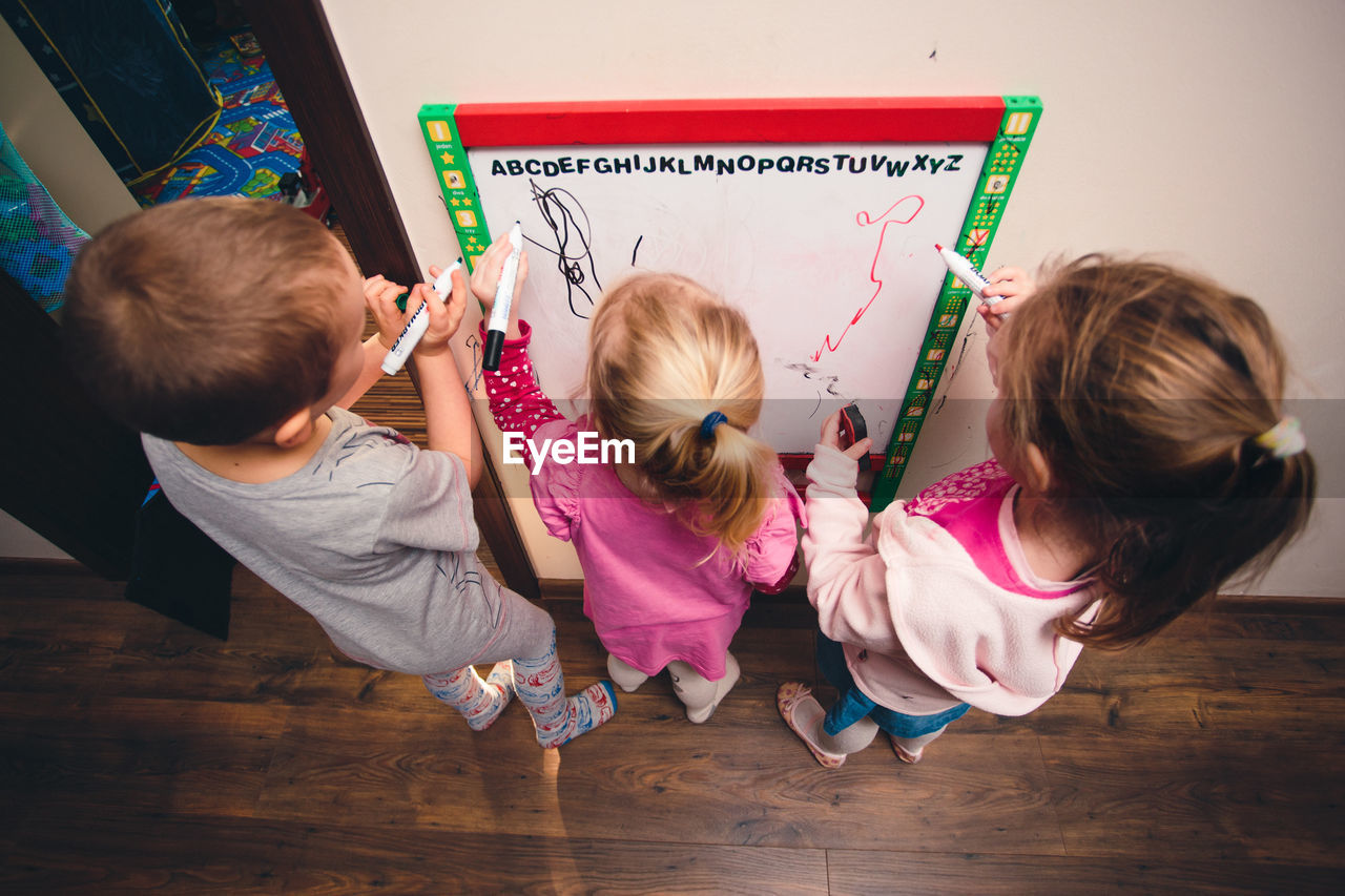 High angle view of siblings writing on whiteboard at home
