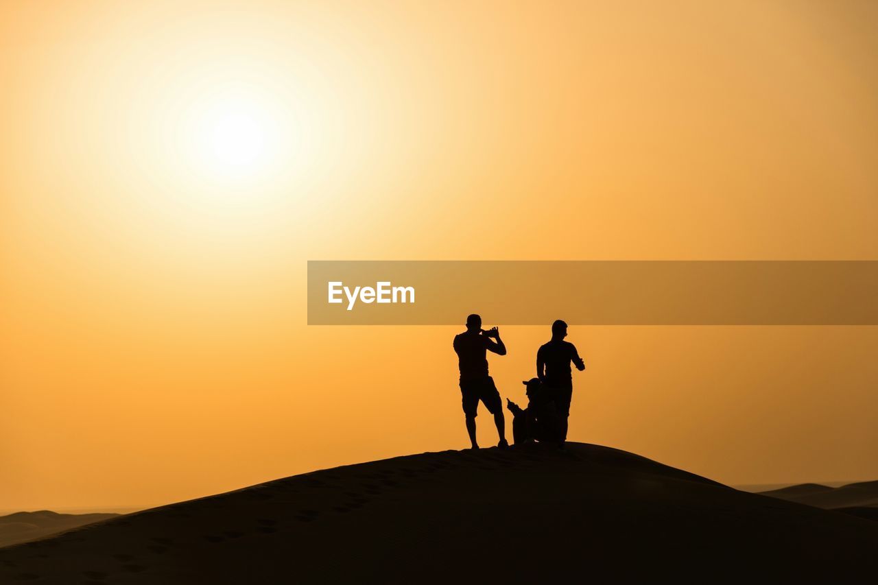 Silhouette men standing on desert during sunset