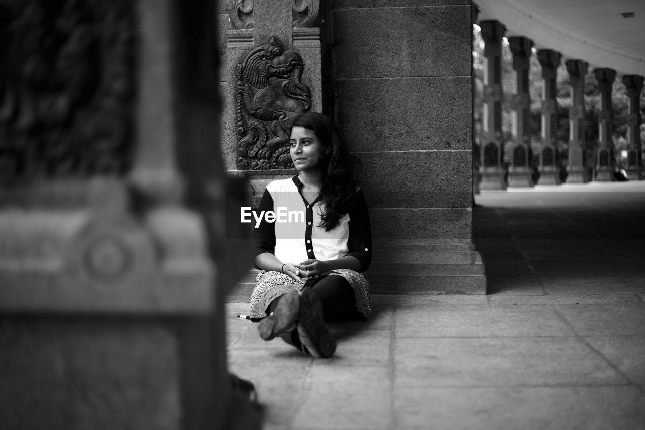 Thoughtful woman looking away while sitting against column