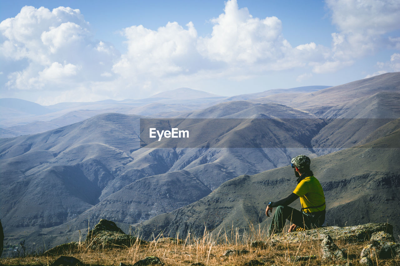 Man sitting on cliff against mountains