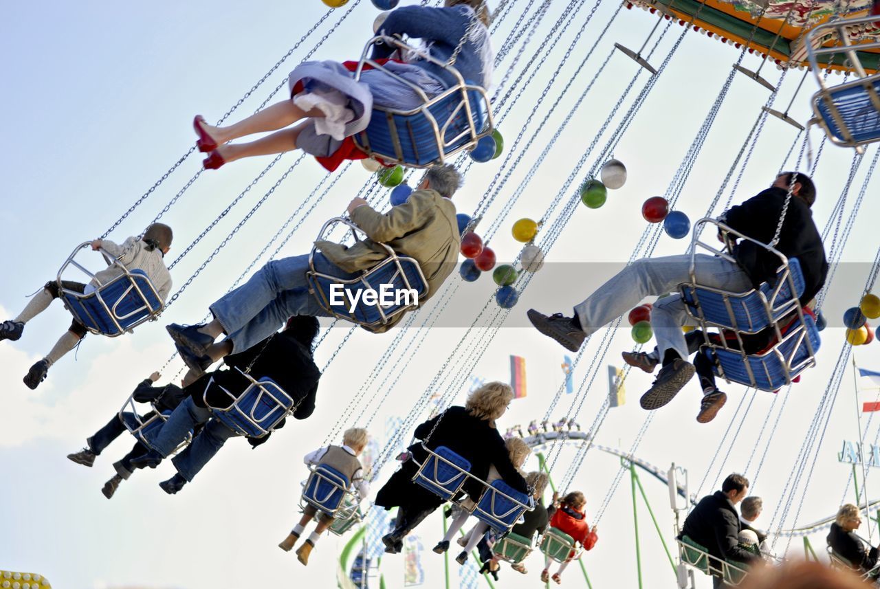 Low angle view of people on chain swing against sky