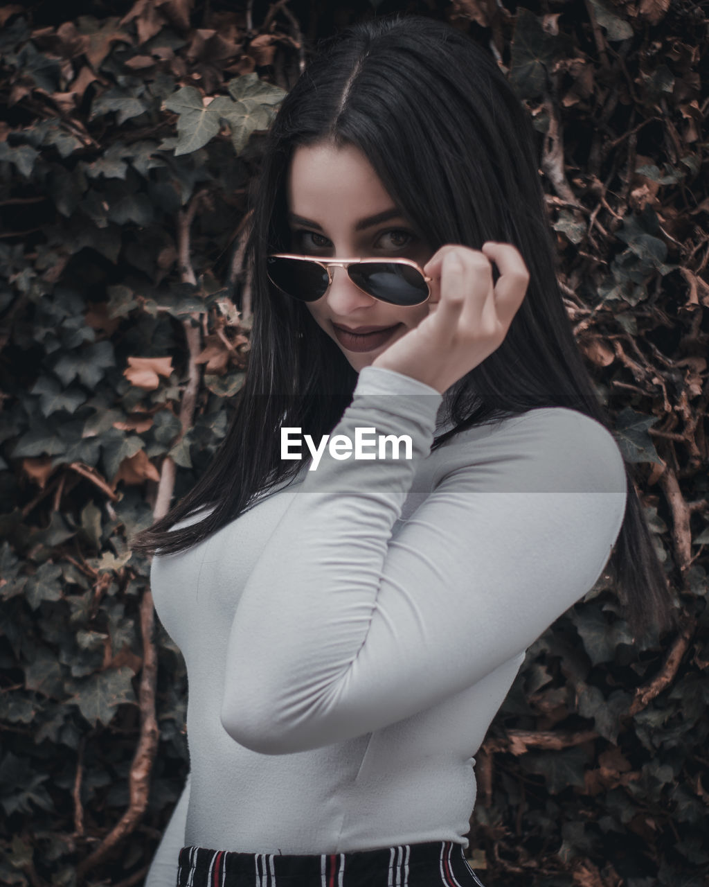 Portrait of beautiful young woman in sunglasses standing against plants