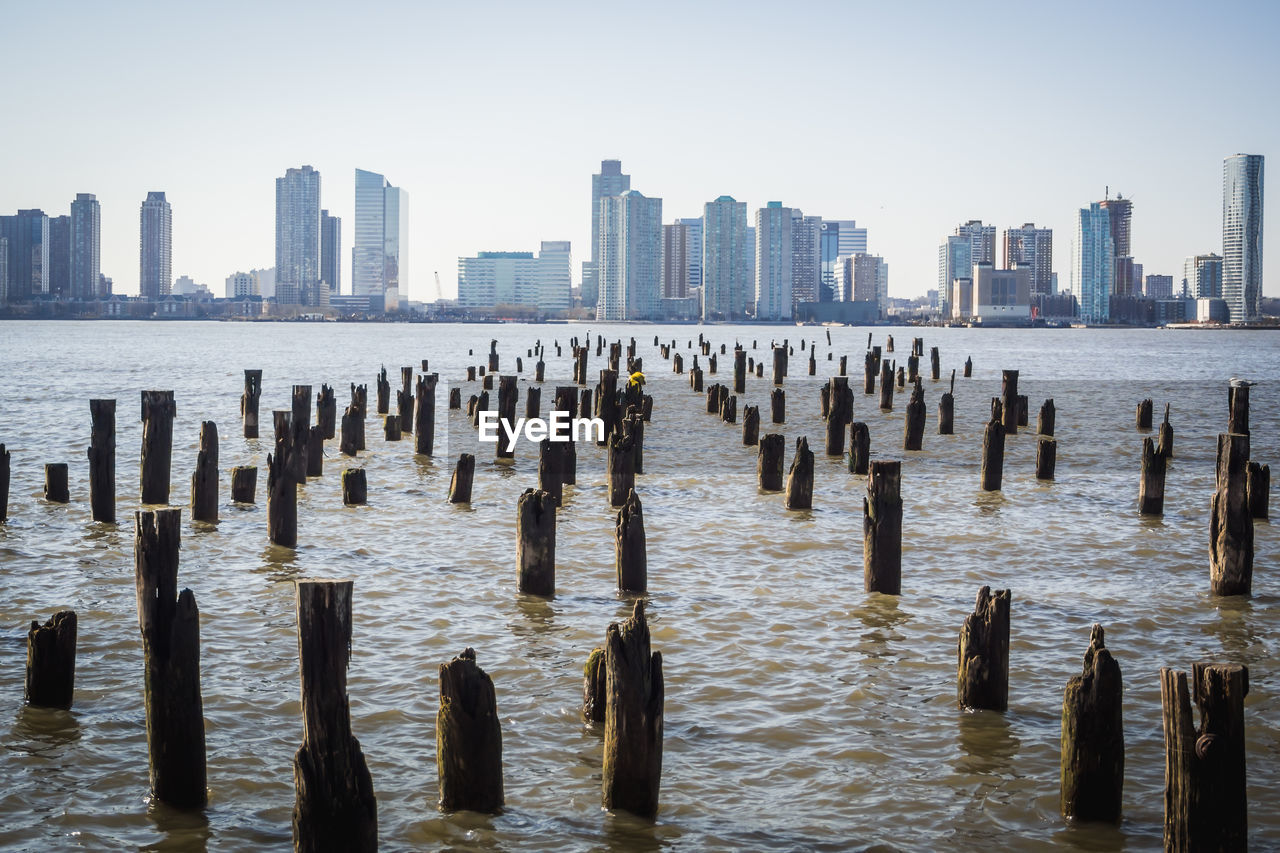 Wooden posts in sea against cityscape in new york city 