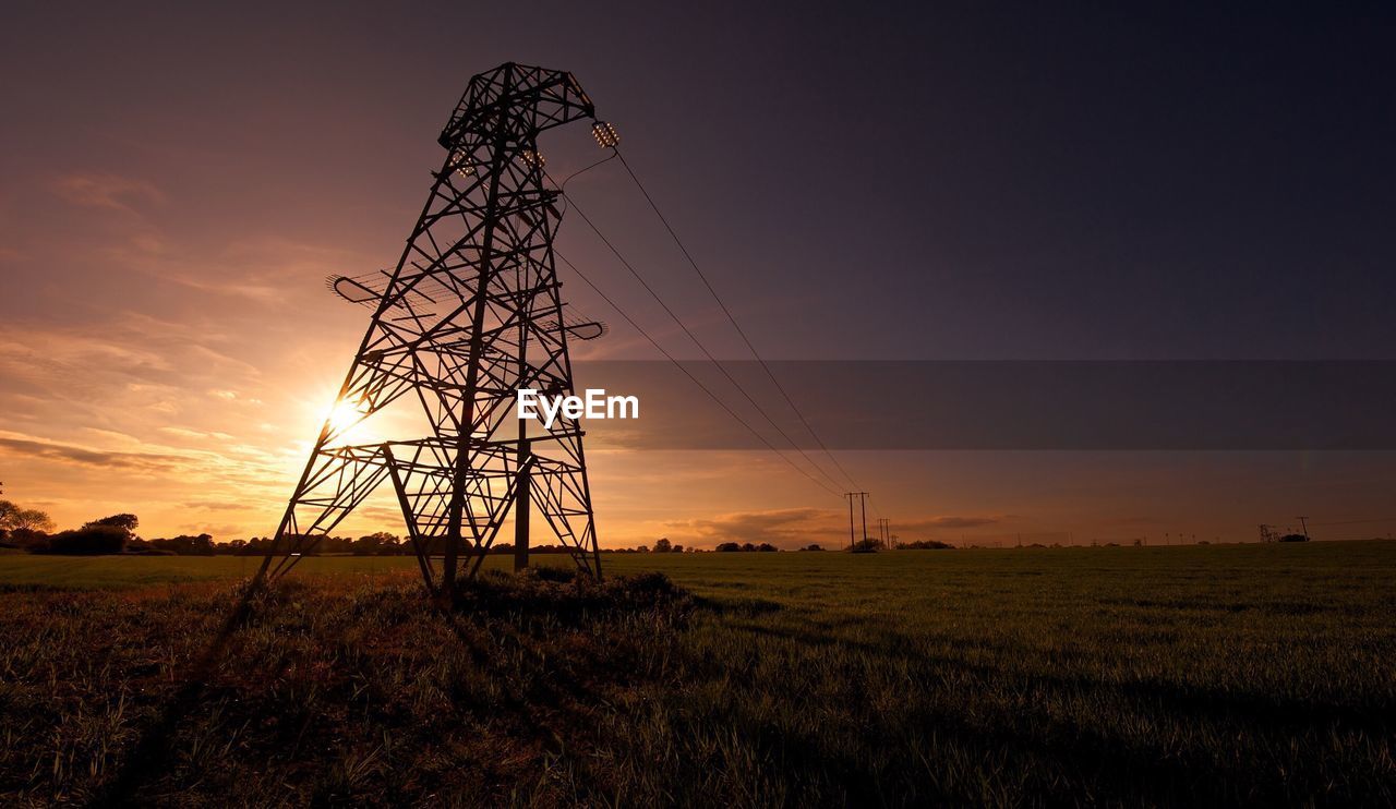 Electricity pylons on field against sky during sunset
