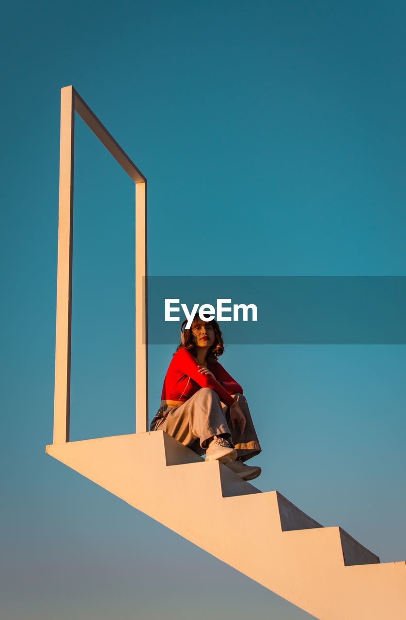 LOW ANGLE PORTRAIT OF YOUNG WOMAN STANDING AGAINST BLUE SKY