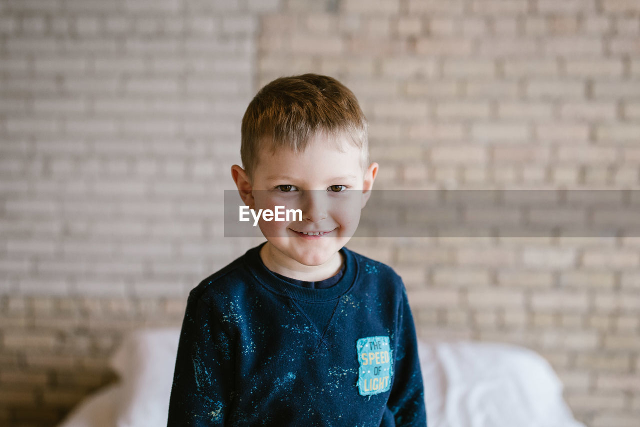 Portrait of smiling boy against brick wall at home