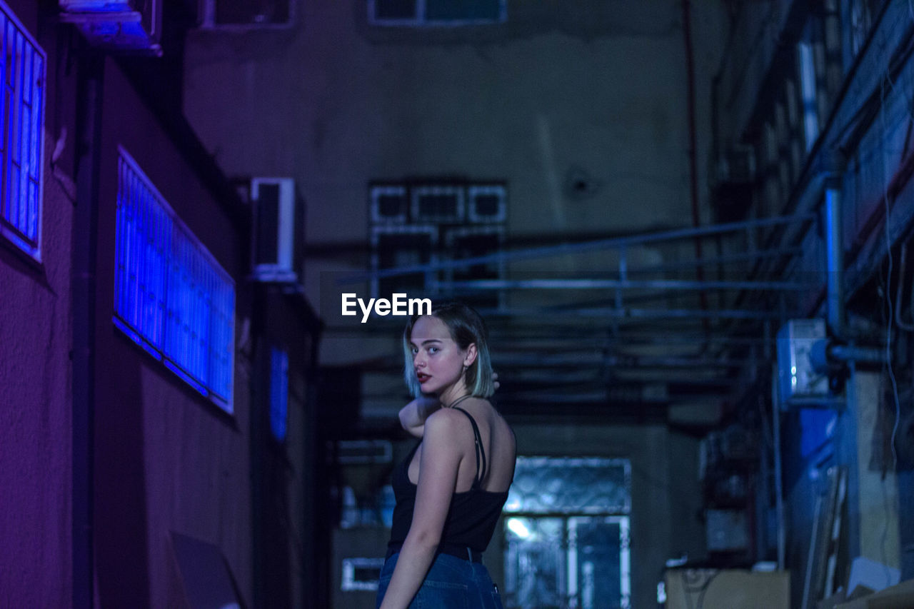 Portrait of woman standing by building at night