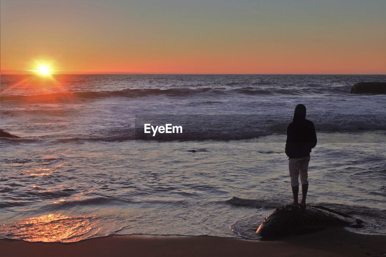 Rear view of man looking at sea during sunset