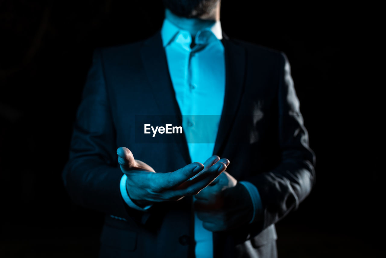 midsection of businessman with arms crossed against black background