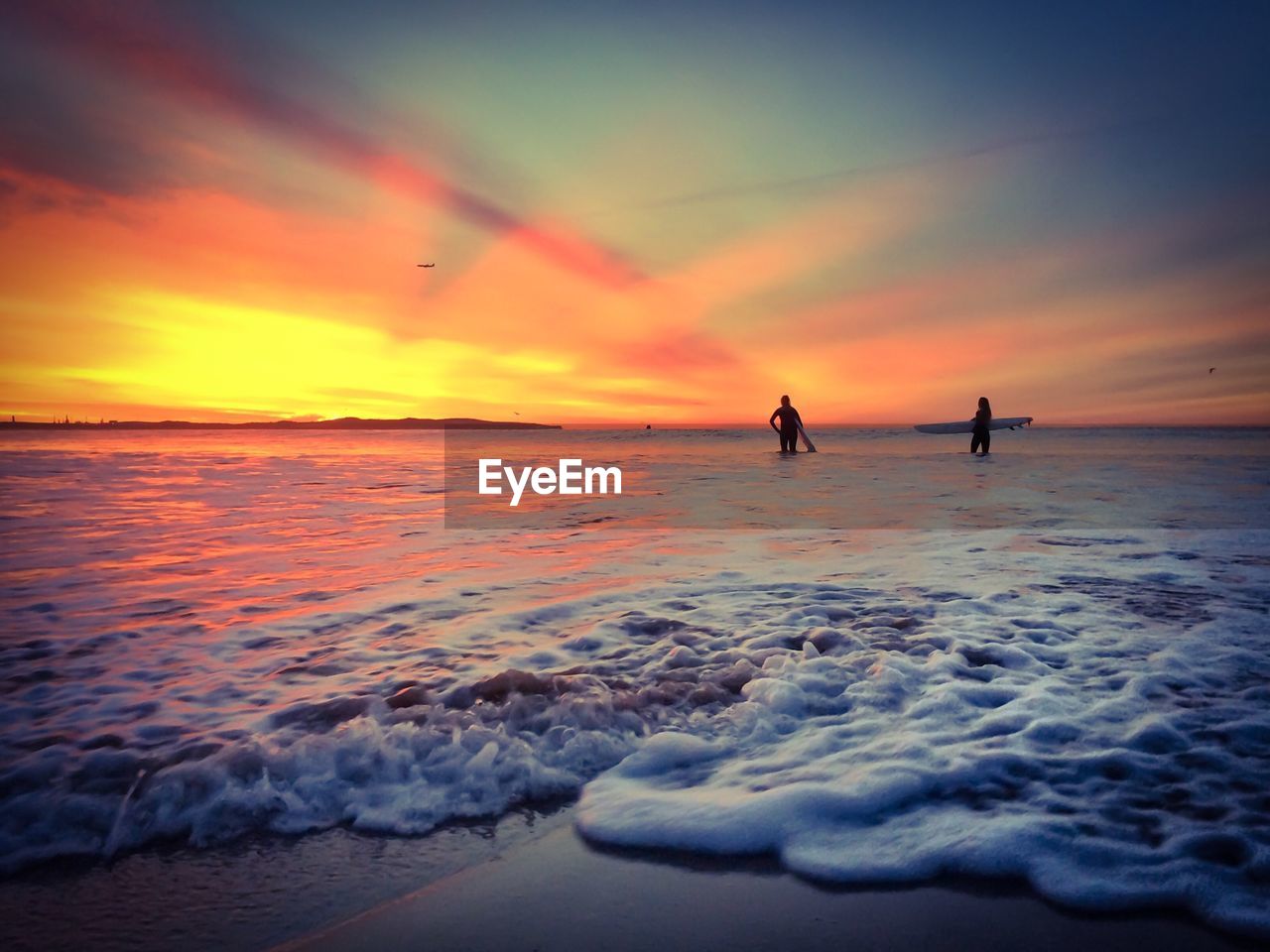 Low angle view of silhouette people with surfboard standing on beach