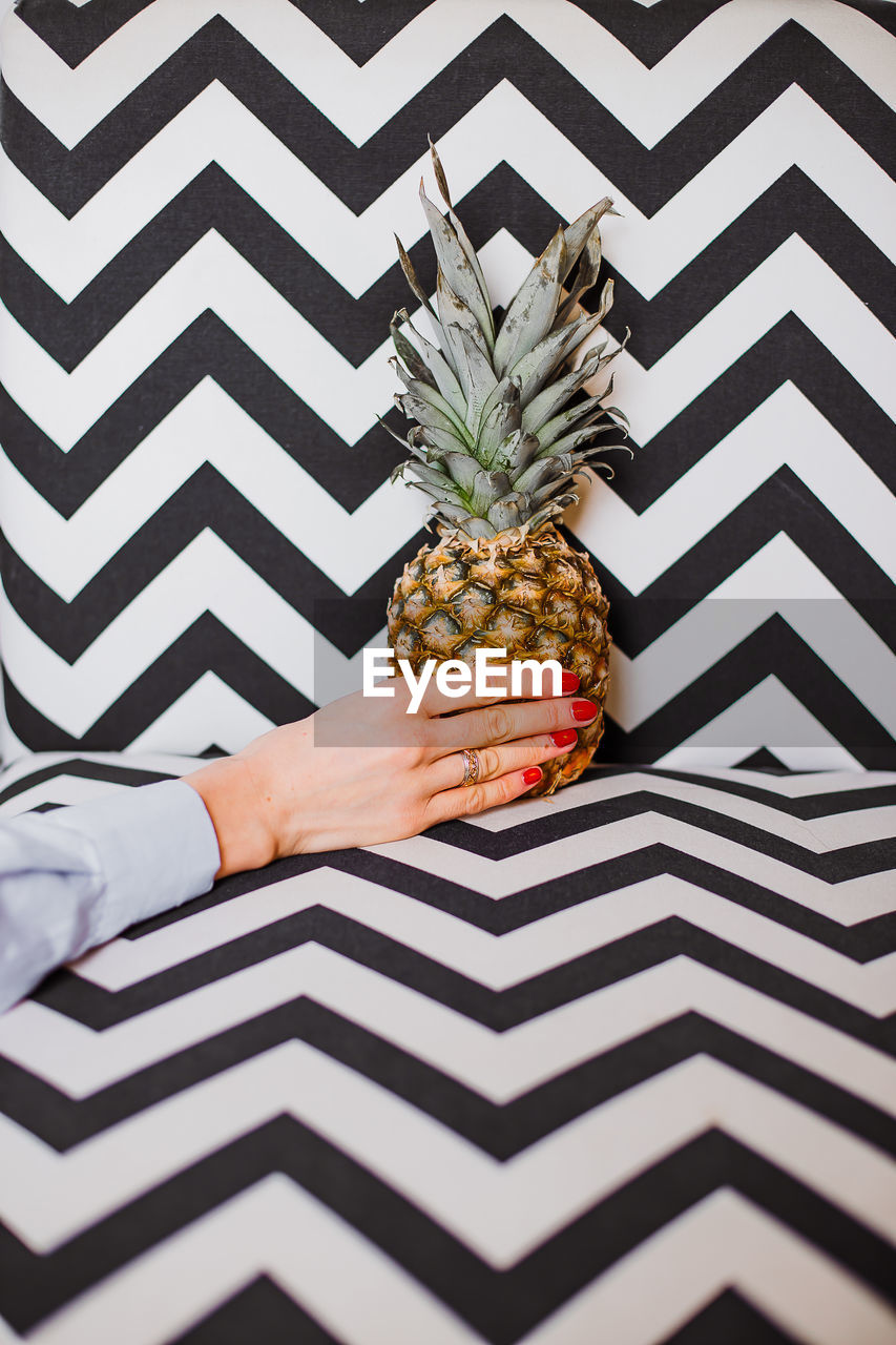 Cropped hand of woman holding pineapple against patterned wall