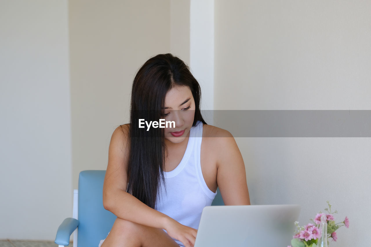 YOUNG WOMAN LOOKING AWAY WHILE SITTING ON LAPTOP