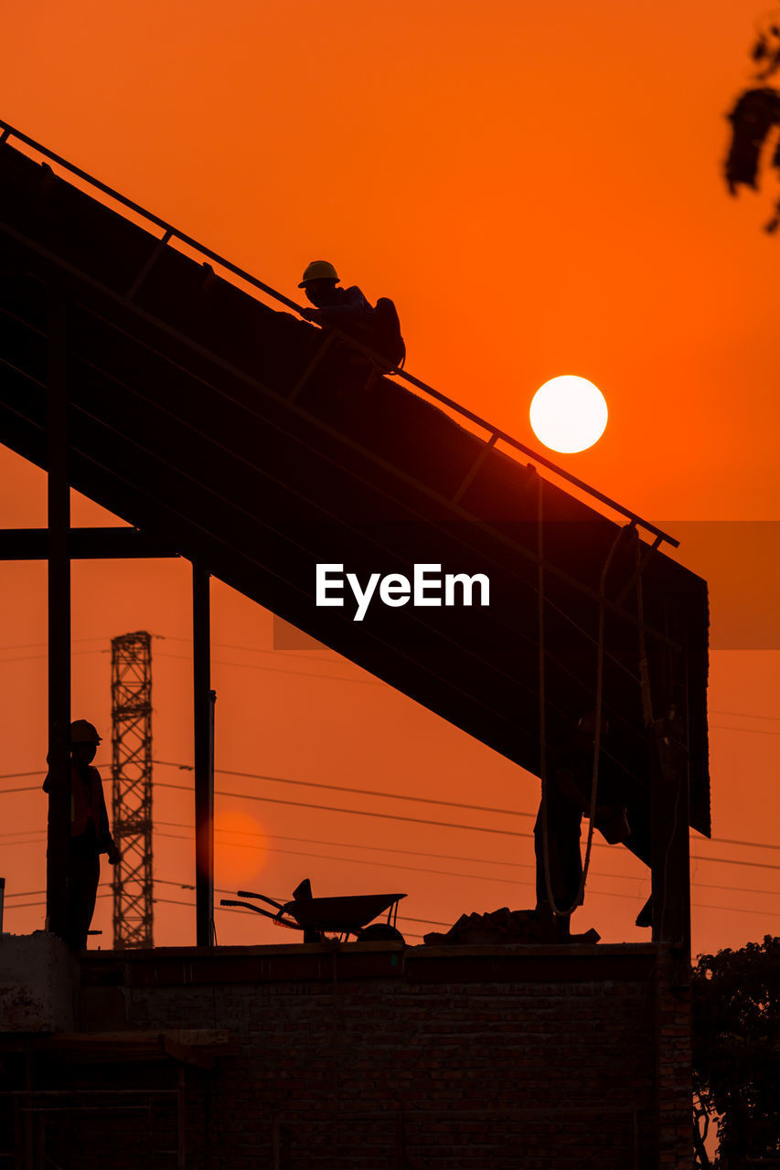 Low angle view of silhouette people on construction against sky during sunset