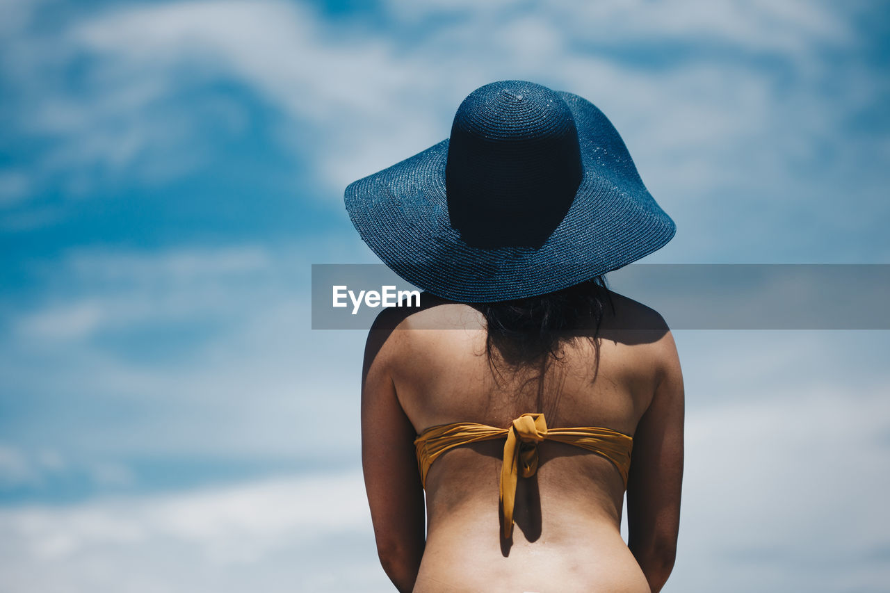 Rear view of woman in bikini wearing hat while standing against sky during sunny day