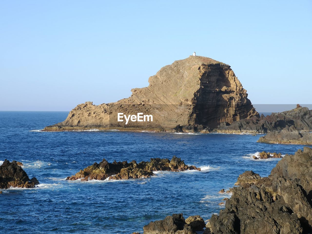 Scenic view of rocks in sea against clear blue sky