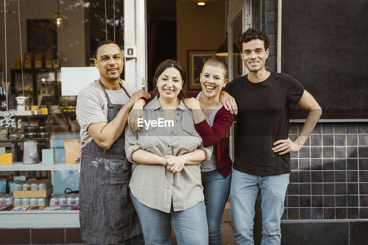 Portrait of happy multiracial male and female business owners standing outside store