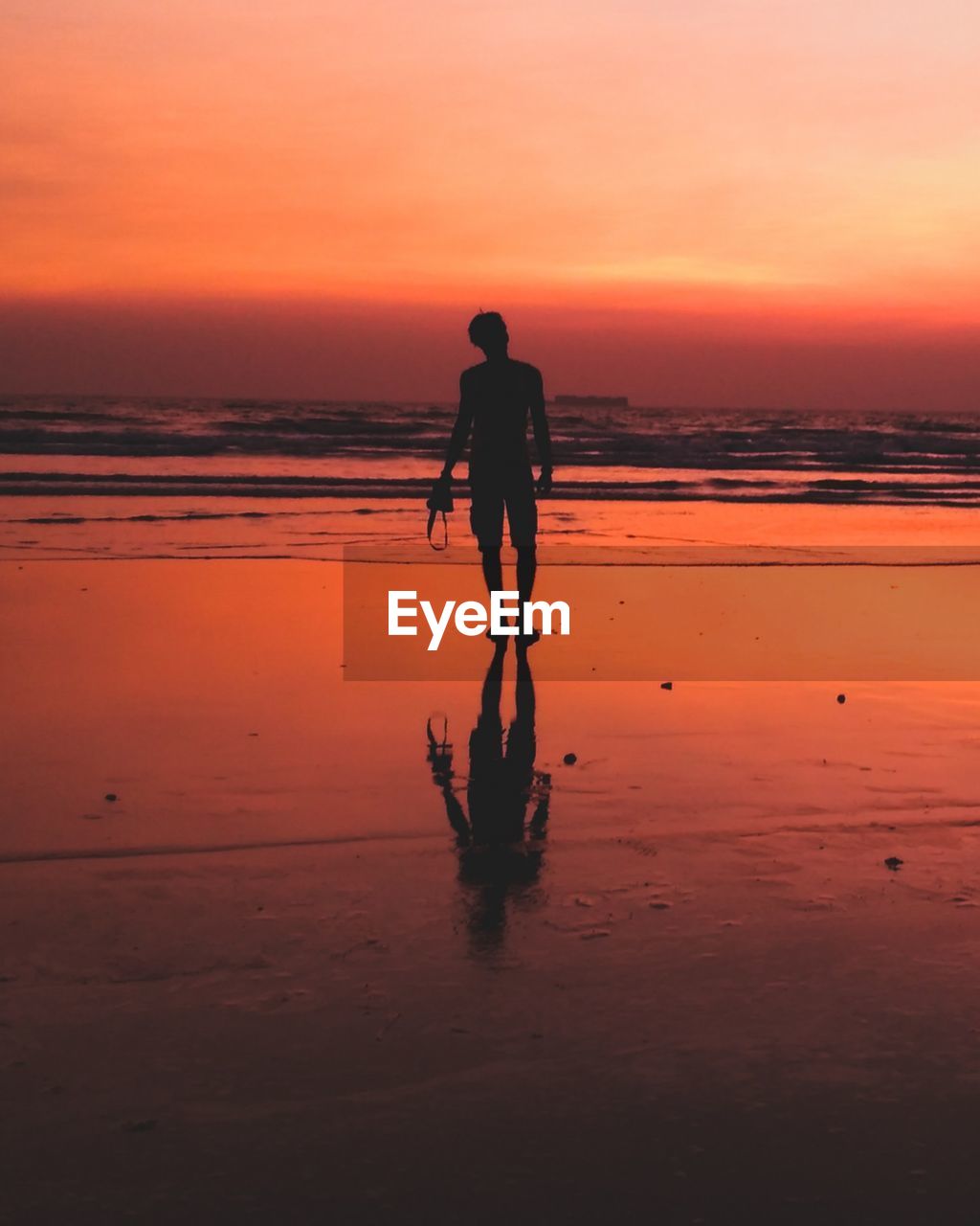 Silhouette man standing on shore at beach against sky during sunset