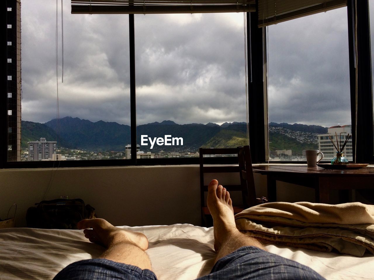 Low section of man relaxing on bed against window