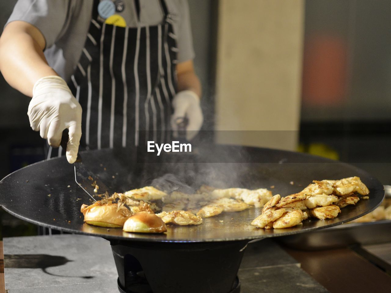 food, food and drink, cooking, kitchen utensil, one person, occupation, dish, freshness, preparing food, chef, fried, midsection, household equipment, heat, cuisine, kitchen, apron, holding, standing, baked, adult, cooking pan, wok, focus on foreground, hand, food and drink establishment, indoors, business, meal, unhealthy eating, working, men, street food, skill, fast food, domestic room, restaurant, meat, frying pan, pan, uniform