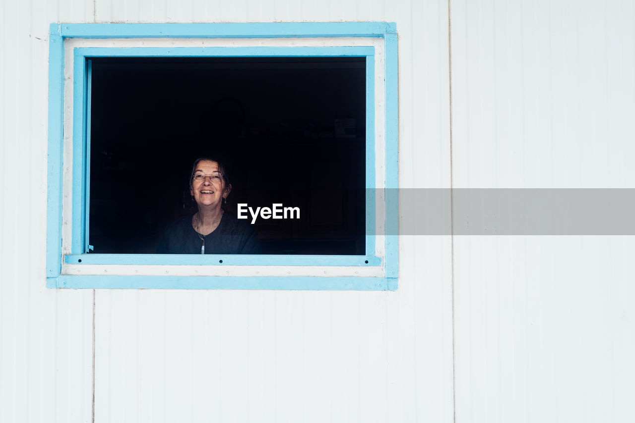 Portrait of smiling young woman looking through window