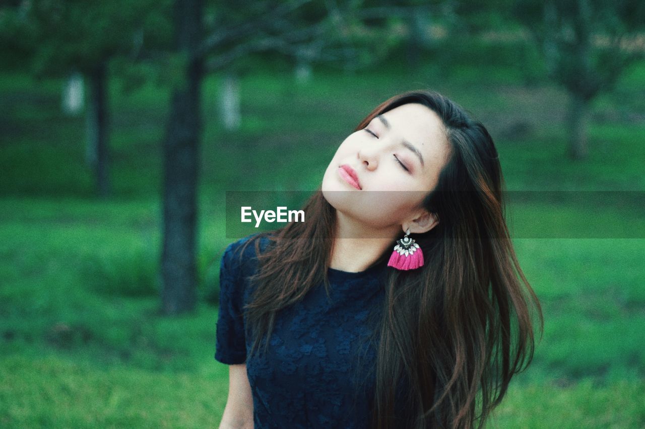 Beautiful young woman with eyes closed standing in forest