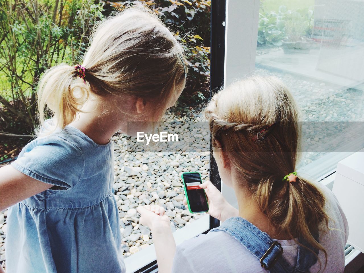 Mother with daughter using phone by window at home