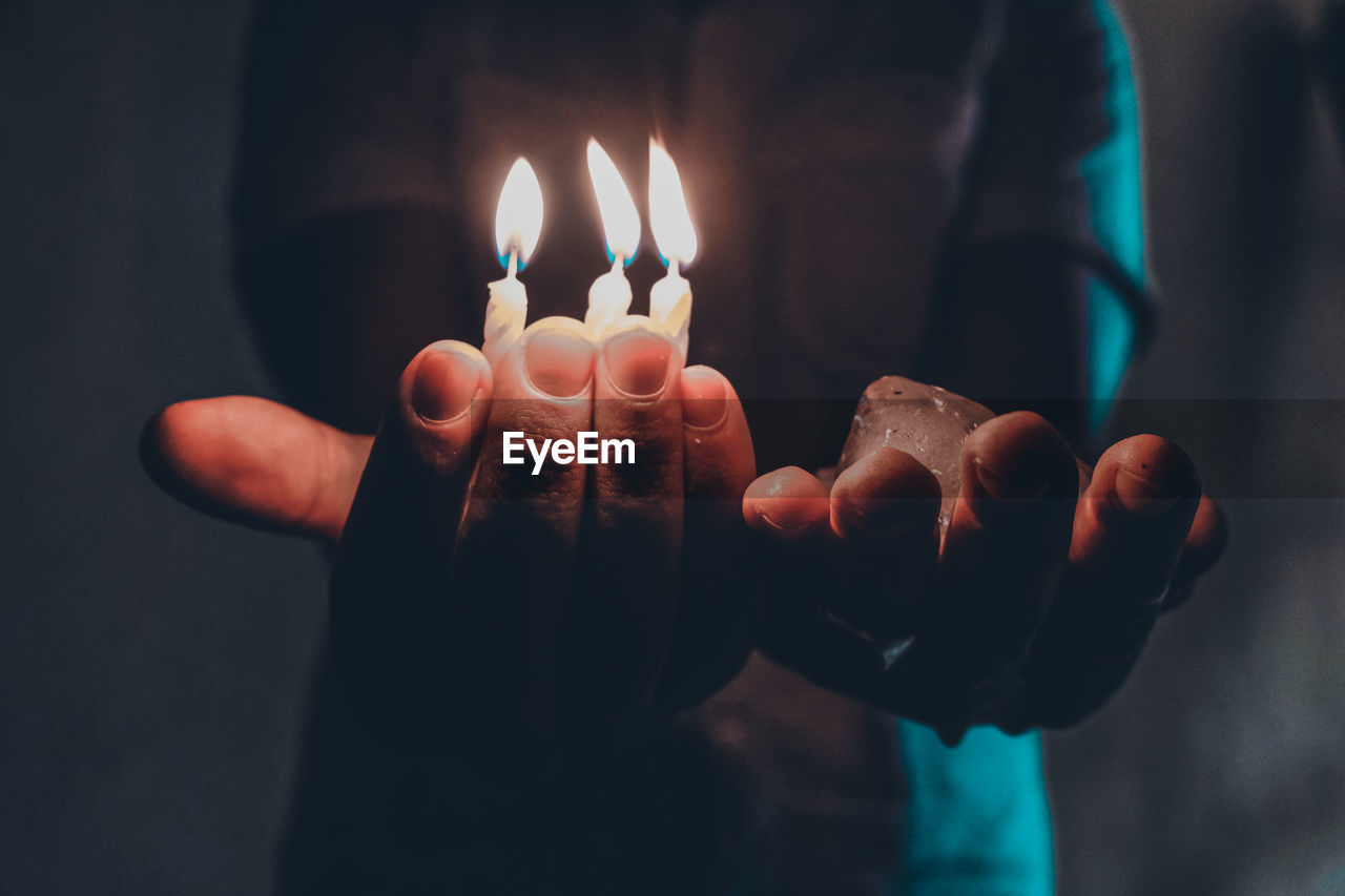 Midsection of man holding burning candles