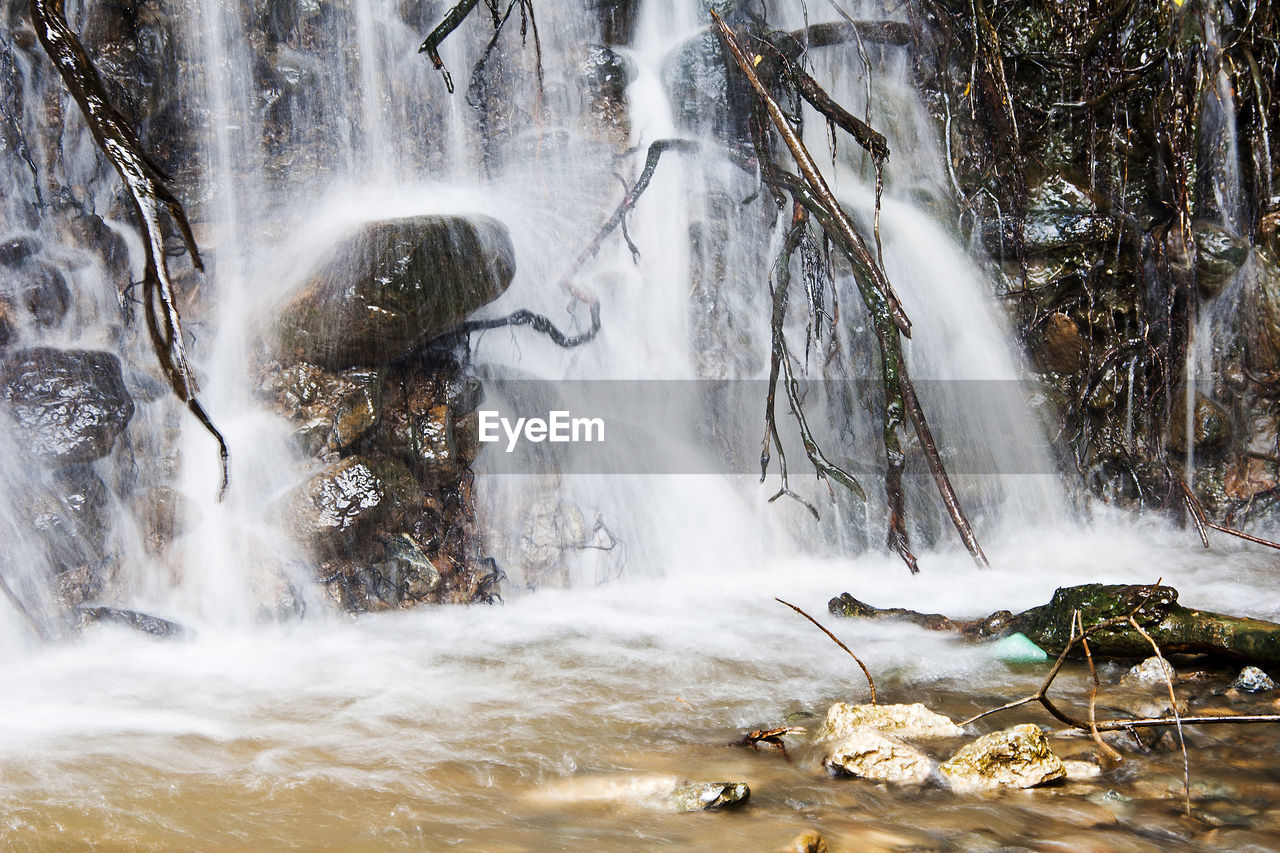 Rains expose tree roots in a small waterfall and drag garbage