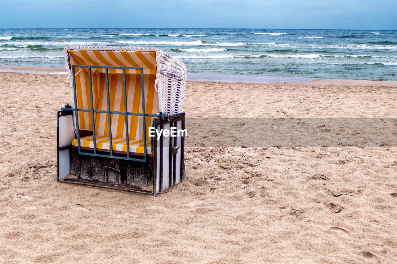 Hooded chair at beach against sky