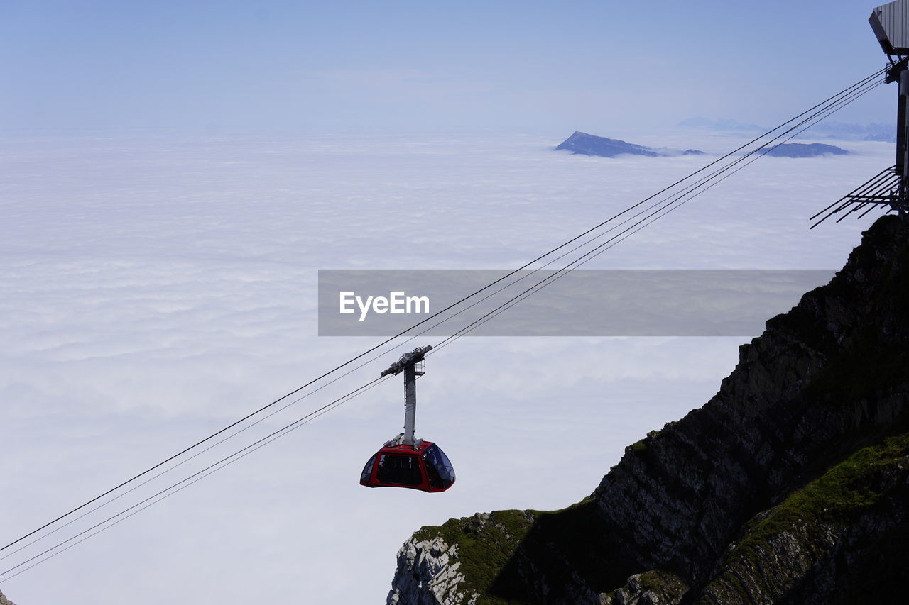 Low angle view of cablecar hanging over clouds against sky