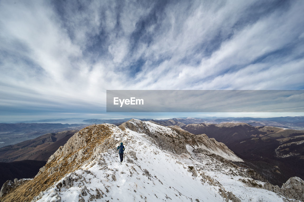 Rear view of woman on snowcapped mountain against cloudy sky