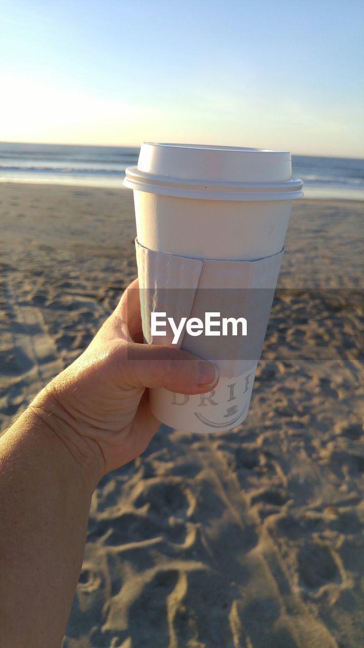Cropped image of hand holding disposable cup at beach