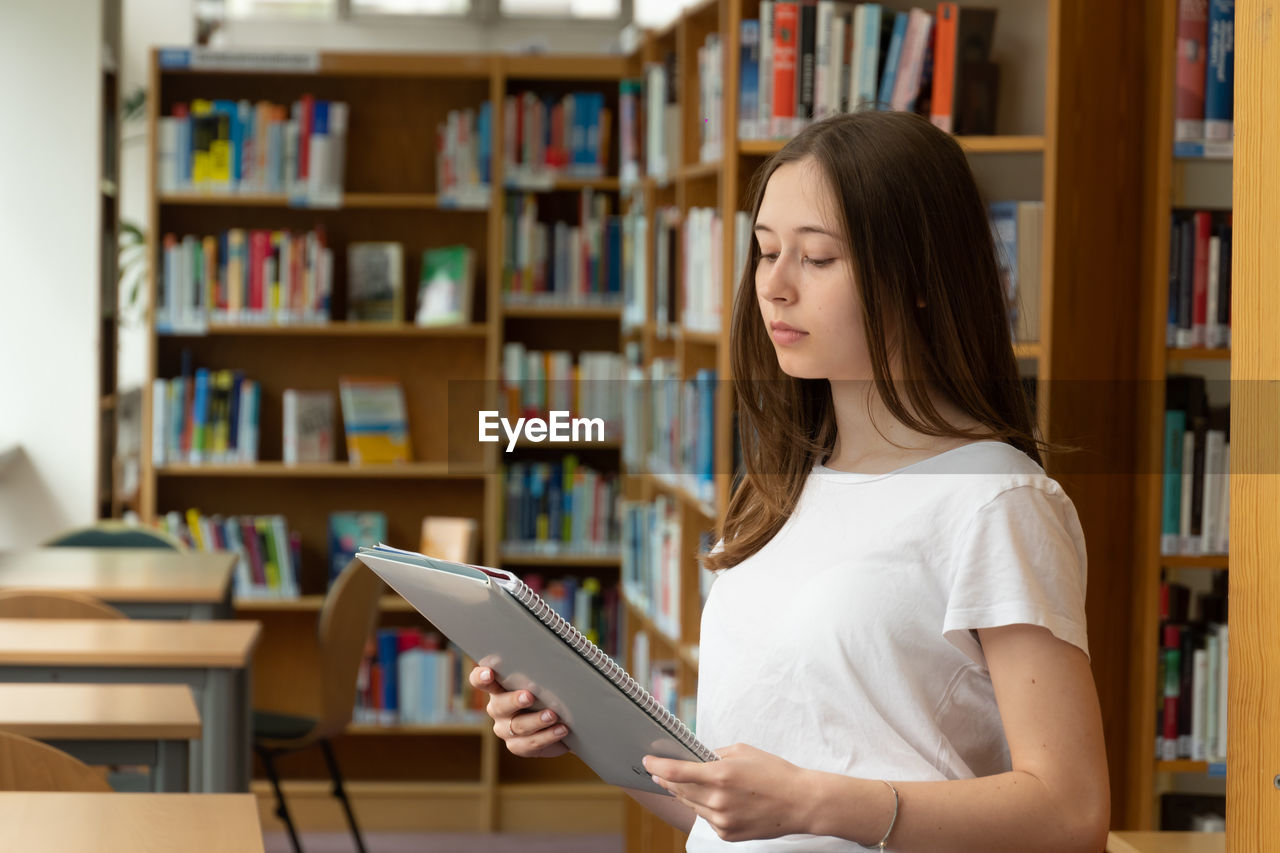 Teenage girl holding file while standing in library