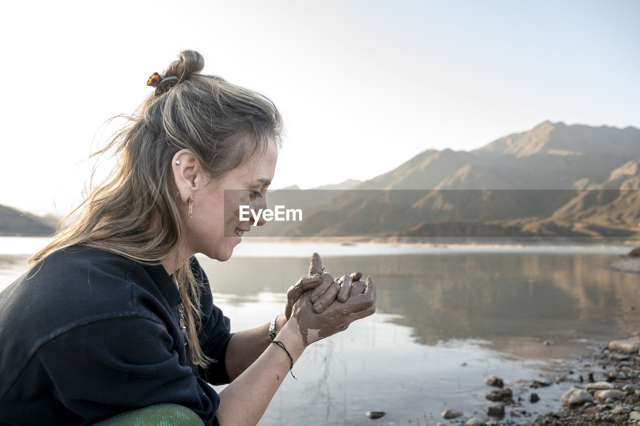 Woman putting mud on hands and face while enjoying outdoors in nature.