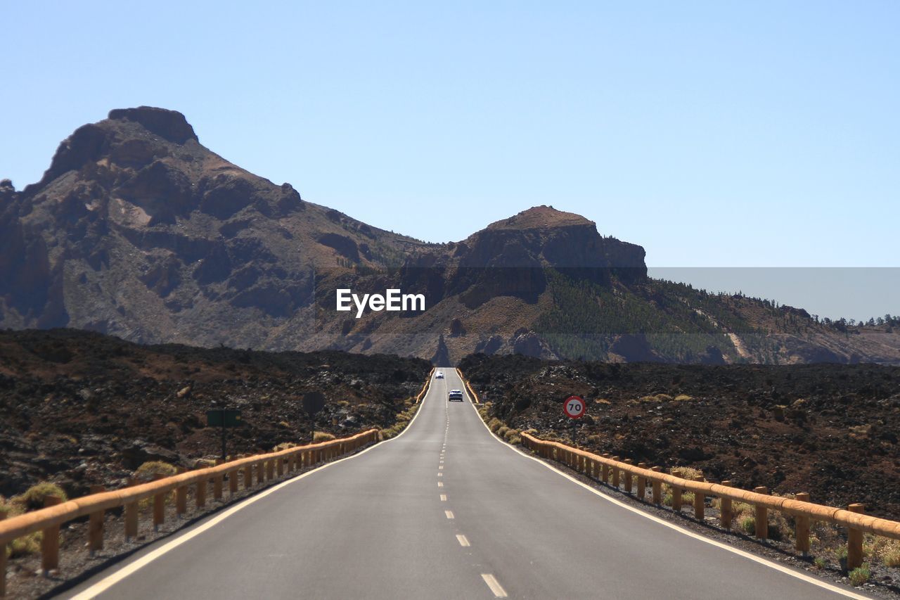 Empty road leading towards mountains against clear sky