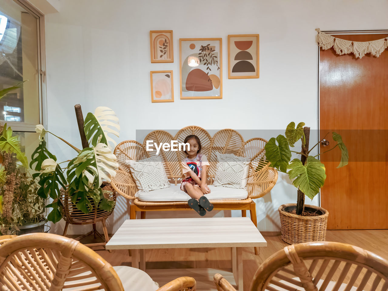 Happy little girl sitting on the rattan couch in a boho interior design.