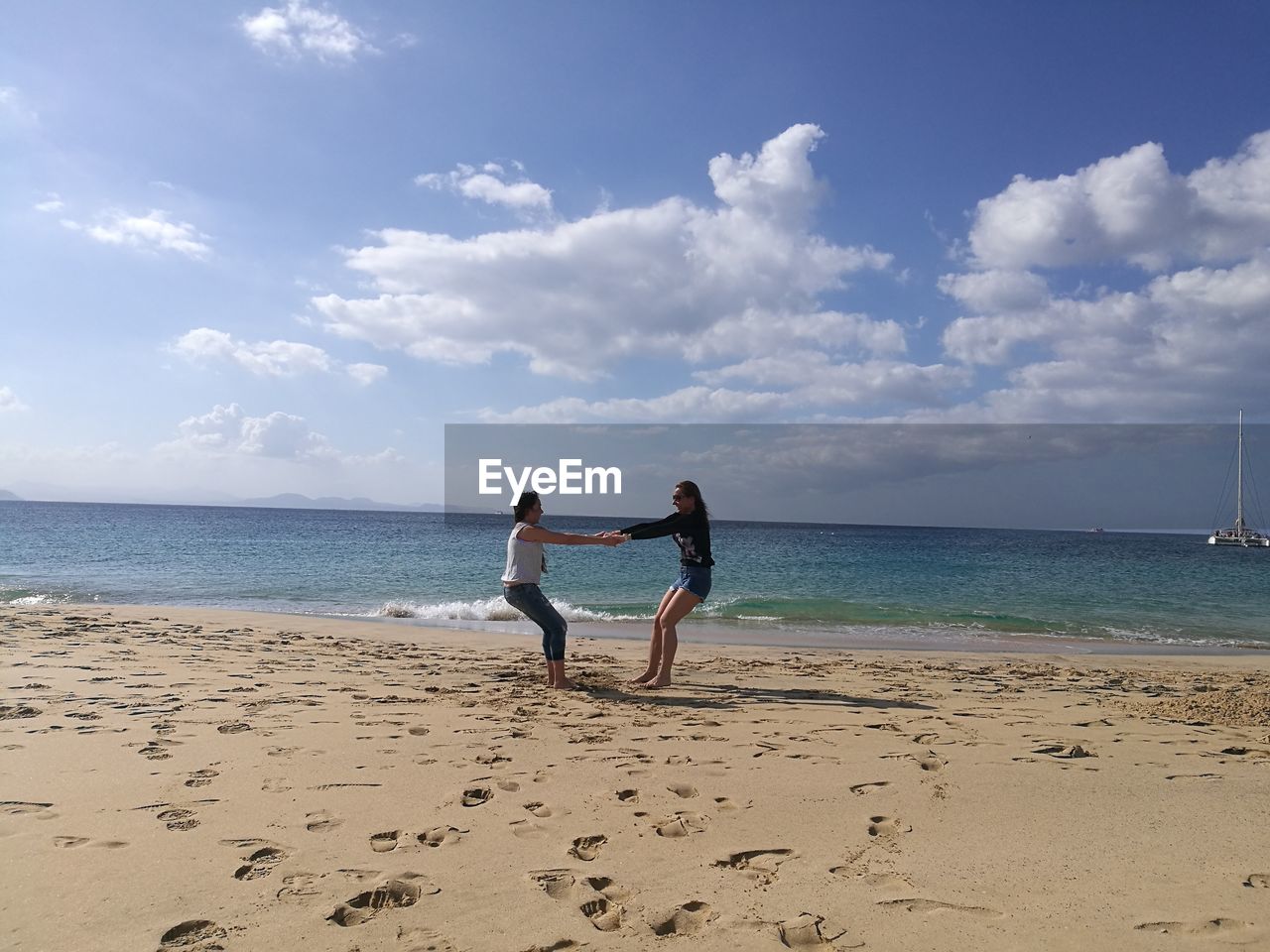 Playful friends on shore at beach against sky