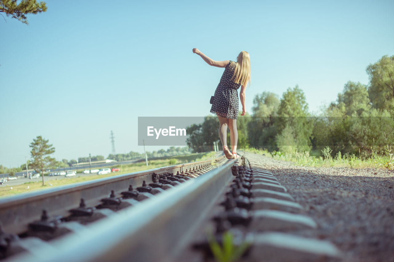 Rear view of woman on railroad tracks against clear sky
