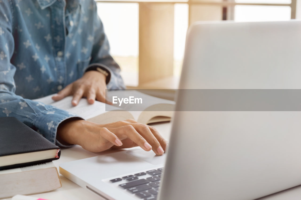 Midsection of woman using laptop while reading book