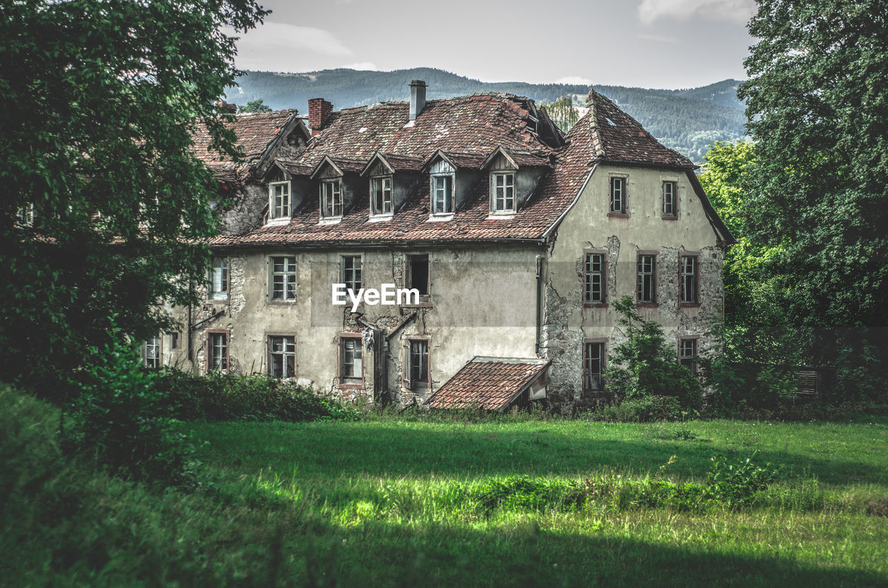 EXTERIOR OF OLD BUILDING BY TREES ON FIELD