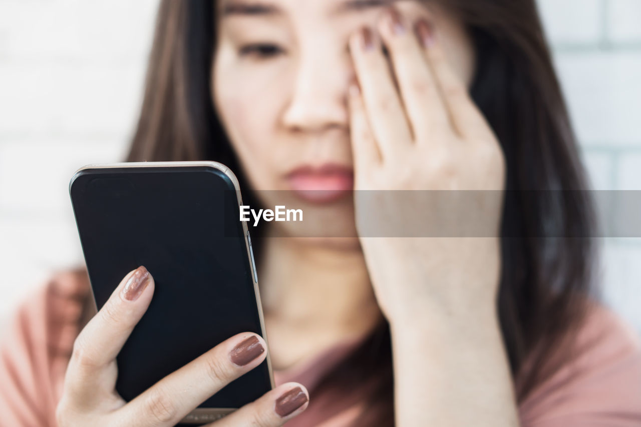 Close-up of woman using mobile phone while covering eye with hand