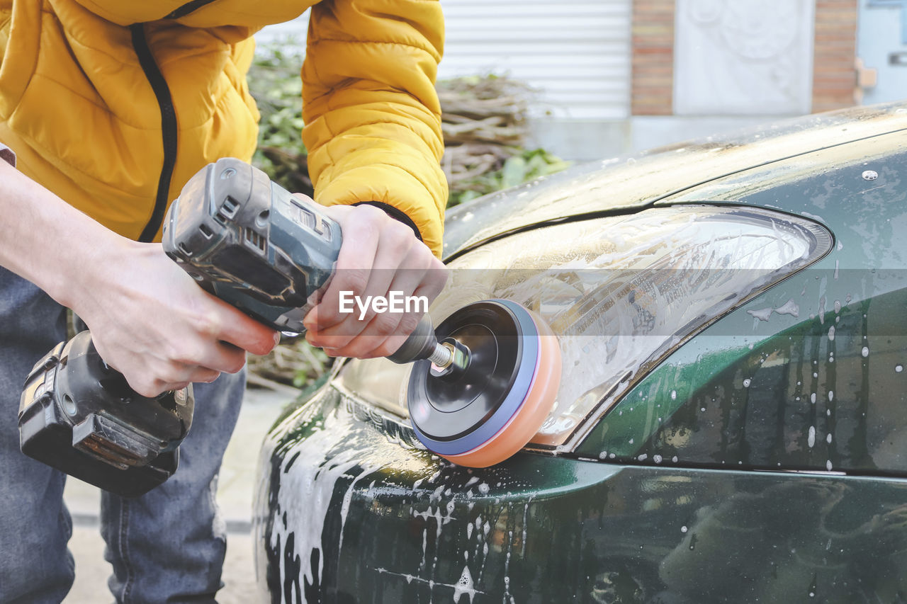 A young man polishes the headlights of a car.